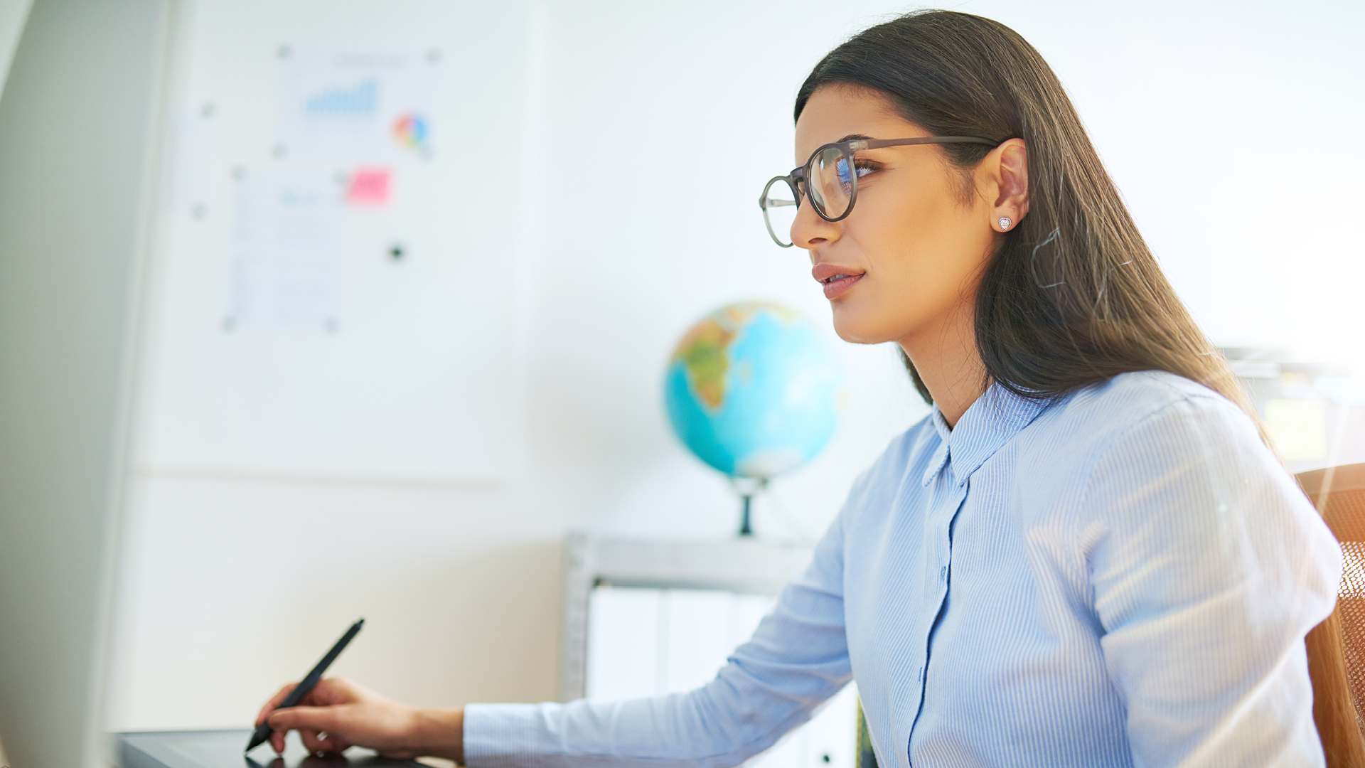 Women sitting at a desk holding a pen with globe in background